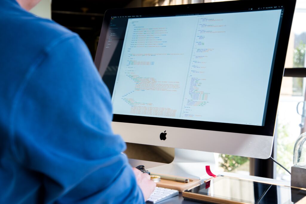 A programmer in a blue shirt coding on an iMac. Perfect for technology or work-related themes.